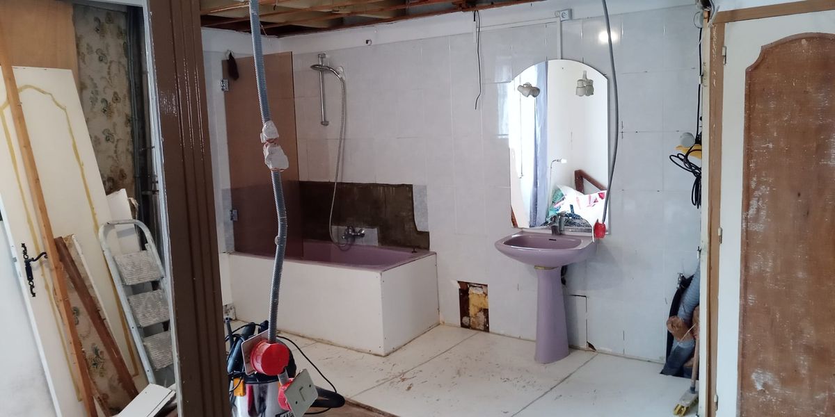 L’ancienne salle de bains : baignoire et lavabo mauves, carrelage blanc, plafond déjà ouvert.