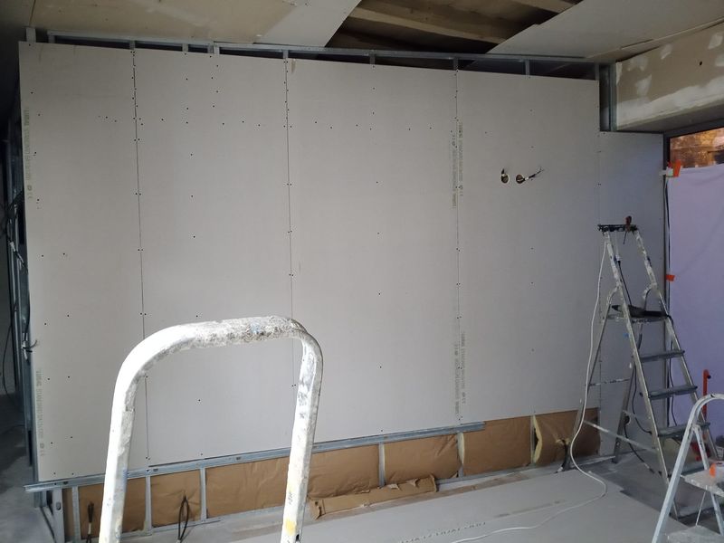 Cloison en plaques de plâtre en cours de fermeture, isolant encore visible en partie basse.