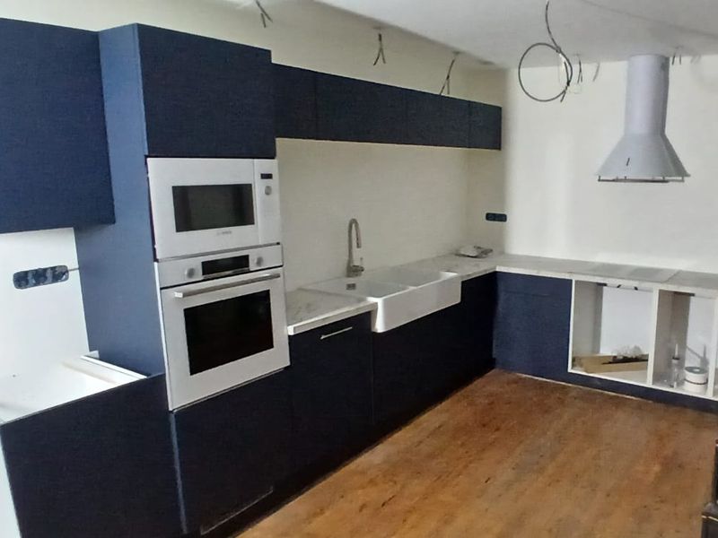 Cuisine en cours de pose : meubles bleu nuit, colonne four, hotte et évier en place, finitions en attente.