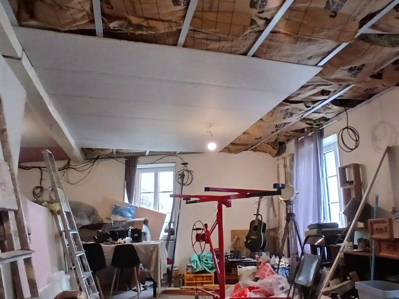 Plafond en cours de remplacement dans une pièce encore meublée : lève-plaque, échelles et meubles se partagent l’espace.