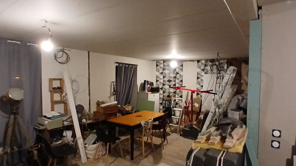 Le séjour pendant les travaux : table, chaises et meubles regroupés au milieu du matériel de chantier.